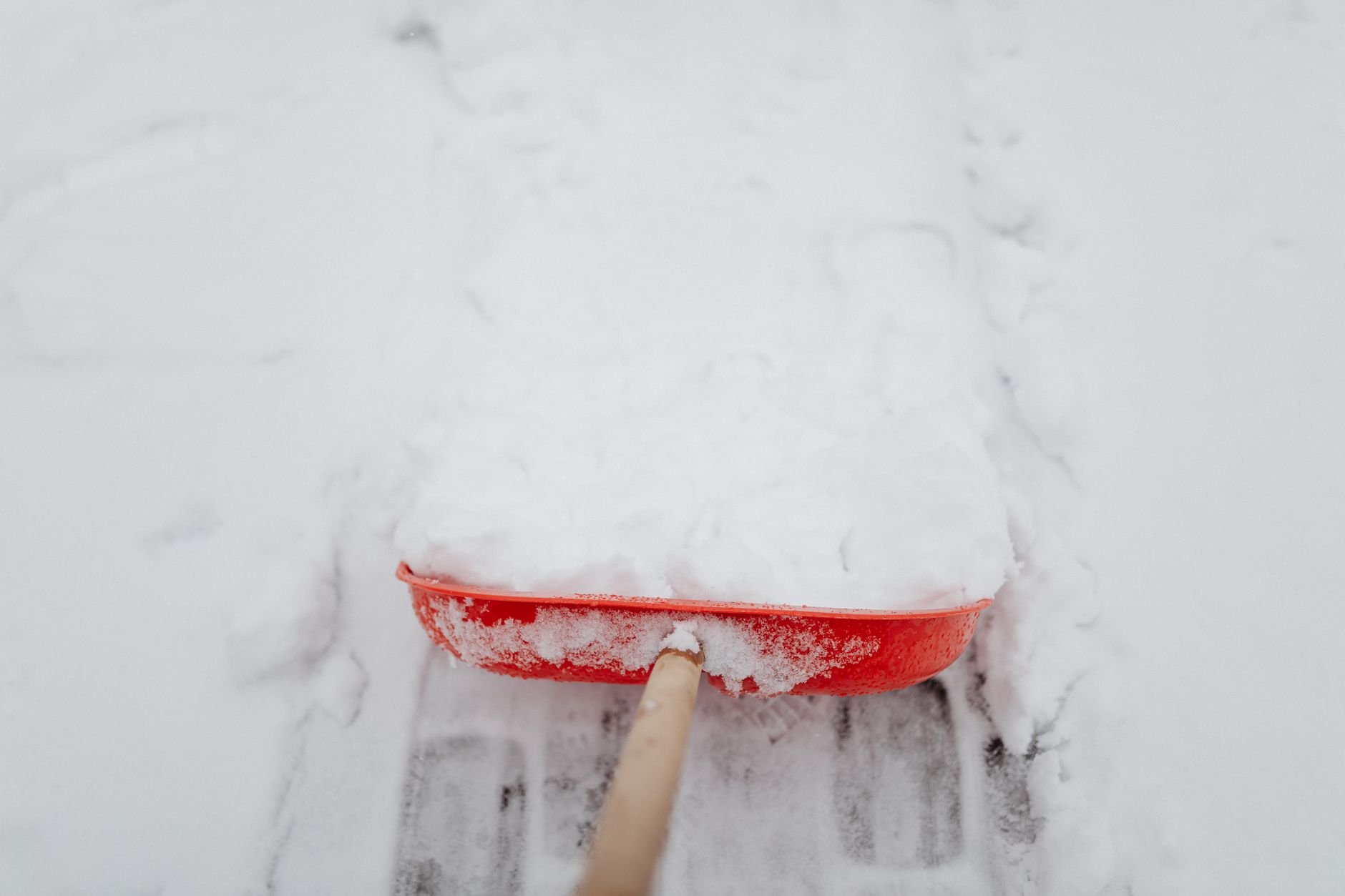Close-up of a red shovel clearing snow from a driveway in winter.